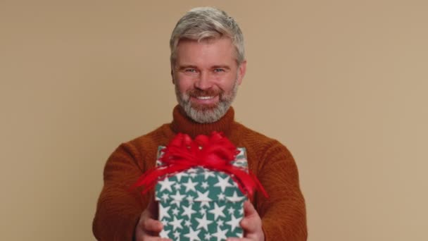 誕生日プレゼントボックスを提示肯定的な笑顔中年の男性は手を伸ばし 現在のキャリアボーナスをラップ提供し パーティーを祝います シニア成熟しました男絶縁一人でベージュスタジオ背景 — ストック動画