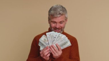 Rich pleased boss mature old man waving money dollar cash banknotes bills like a fan, success business career, lottery winner, big income, wealth. Senior middle-aged guy isolated on beige background
