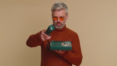 Hey sen, beni ara. Orta yaşlı bir adam 80 'lerin modası geçmiş eski moda telefonuyla konuşuyor. Reklamlarda beni geri ara diyor. Yaşlı yetişkin adam bej renkli stüdyo arka planında tek başına izole edilmiş.