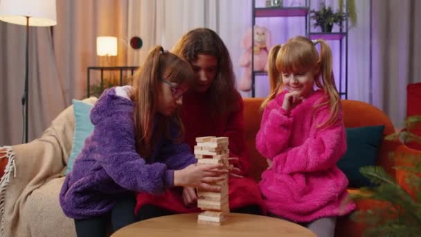 十几岁的女孩和蹒跚学步的孩子姐姐们用木砖建造塔楼 输掉了棋盘比赛 三个兄弟姐妹 孩子们 孩子们 朋友们 玩着塔楼 在家里的游戏室里玩着方块 — 图库视频影像