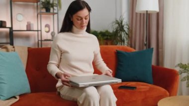Young brunette woman freelancer at home living room sitting on couch, opens laptop computer start working. Girl works on notebook, sends messages, makes online purchases, watching movies, working