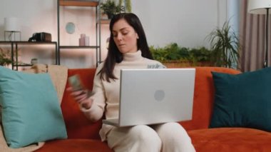 Planning budget. Rich happy young woman counting money cash use laptop computer calculate domestic bills at home room. Joyful girl satisfied of income earnings, saves money for planned vacation, gifts