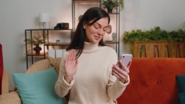 Young woman blogger taking selfie on smartphone, communicating video call online with subscribers. Girl influencer recording video vlog story for social media at home apartment living room on couch