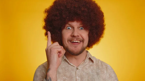 Eureka. Inspired man with lush Afro hairstyle coiffure pointing finger up with open mouth, showing Eureka gesture, solution, idea, inspiration, answer. Young guy isolated on yellow studio background
