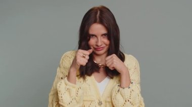 Funny happy pretty woman trying to fight at camera, shaking fist, boxing with expression, punishment, disappointment, rage, quarrel. Young adult girl isolated alone on gray studio wall background