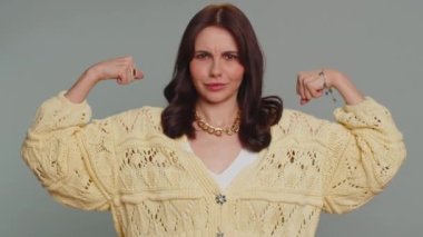 I am strong and independent. Proud success woman showing biceps and looking confident, feeling power strength to fight for rights energy to gain success win. Young adult girl on gray studio background