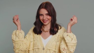 Cheerful rich millennial woman showing wasting or throwing money around hand gesture, more tips dreaming about big profit body language. Young millionaire girl isolated on gray studio wall background
