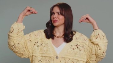 Bored pretty young woman in cardigan showing blah blah gesture with hands, has not interested in the conversation, gossips, empty promises, lier. Millennial girl isolated on gray studio background