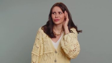 I cant hear you. What. Young woman trying hear you, looking confused and frowning, keeping arm near ear for louder voice, asking to repeat to hear information, deafness. Girl on gray studio background