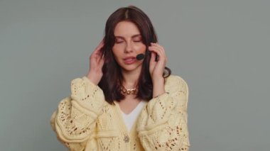 Gülümseyen, kulaklık takan güzel bir kadın, serbest çalışan, çağrı merkezi ya da destek operatörü yardım hattı, müşteriyle ya da meslektaşıyla konuşmak, iletişim desteği. Gri arka planda genç bir kız