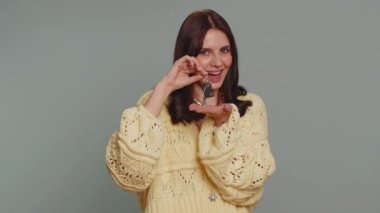 Pretty young woman in cardigan real estate agent lifting hand showing the keys of new home house apartment, buying, renting property, mortgage loan. Happy girl isolated on gray studio background