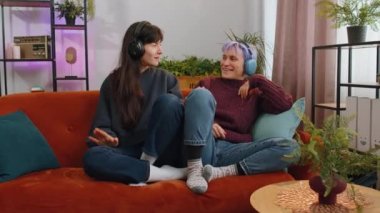 Happy relaxed overjoyed young lesbian women family couple or girls friends in wireless headphones dancing choosing listening favorite energetic disco rock n roll music song on home couch. LGBT people