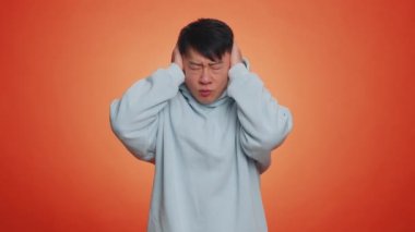 Dont want to hear and listen. Frustrated annoyed irritated asian man covering ears gesturing No, avoiding advice ignoring unpleasant noise loud voices. Handsome chinese guy alone on orange background