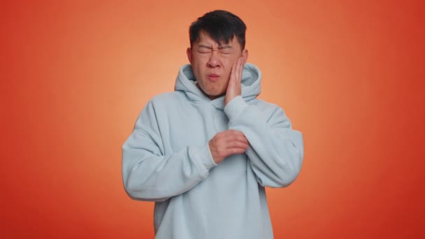 歯痛の虫歯や歯肉炎に苦しむアジア人の男は歯医者の任命歯茎の病気を待っている ハンサムな中国人男性屋内スタジオショット孤立したオンオレンジの背景 — ストック動画