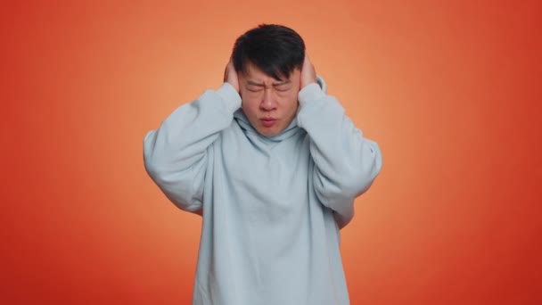 不想听 不想听 沮丧而烦躁的亚裔男人捂住耳朵做手势表示不 避免建议忽略讨厌的噪音 有橙色背景的英俊的中国男人 — 图库视频影像