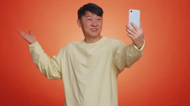 亚洲男子旅行博客 在智能手机上自费 在线与家人或朋友交流视频通话 现场翻译流 漂亮的中国男人 背景是橙色的 在室内 — 图库视频影像