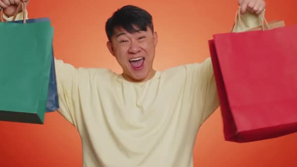 Homem Asiático Mostrando Sacos Compras Descontos Publicitários Sorrindo Olhando Espantado — Vídeo de Stock