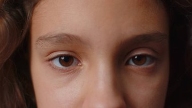 Extreme close-up macro portrait of smiling girl face. Teen beautiful kids eyes, looking at camera. Brown eyes of brunette female child model. Young positive cute children opening wide her closed eyes