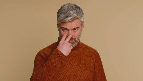 I am watching you. Caucasian man in sweater pointing at his eyes and camera, show I am watching you gesture, spying on someone. Senior adult middle-aged guy isolated alone on beige studio background