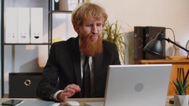 Tired ill young businessman suffering from headache problem tension and migraine, stress at home office desk workplace. Bearded freelancer broker worker man works on laptop notebook. Overworking