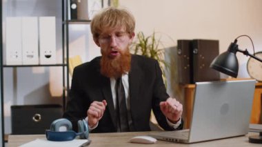 Happy relaxed overjoyed young businessman working on laptop computer at home office wearing headphones listening favorite energetic disco music on smartphone. Freelancer man relaxing, taking a break