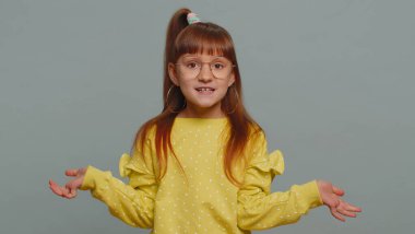 I dont know what to say. Confused young toddler school girl feeling embarrassed about ambiguous question having doubts no idea, being clueless and uncertain. Teen female child kid on gray background