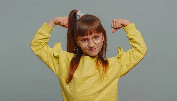 I am strong and healthy. Young toddler girl in glasses showing biceps and looking confident feeling power strength to fight for rights, energy to gain success win. Preteen child kid on gray background