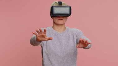 Çevrimiçi oyun uygulaması oynamak için kulaklık kullanan genç bir kadın. Sanal gerçeklik 3D 360 video içeriği izliyor. Stüdyo pembe arka planda VR gözlüklü beyaz bir kız. Gelecekçi teknoloji