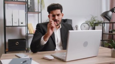 Indian young businessman working on laptop computer shakes finger and saying No be careful scolding and giving advice to avoid danger mistake disapproval sign at home office. Confident freelancer man