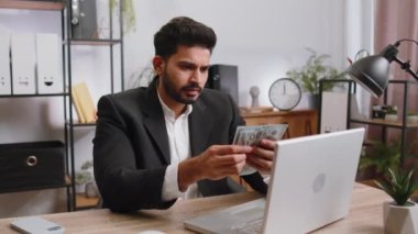 Bilgisayarda çalışan zengin Hintli iş adamı nakit para sayıyor, iş yerindeki gelir gelirlerini hesaplıyor. Profesyonel menajer serbest çalışan adam. İş adamları. İstihdam mesleği