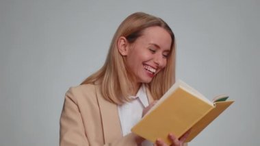 Happy woman in formal suit reading funny interesting fairytale story book, leisure hobby, knowledge wisdom, education, learning, study, wow. Business girl isolated alone on gray studio wall background
