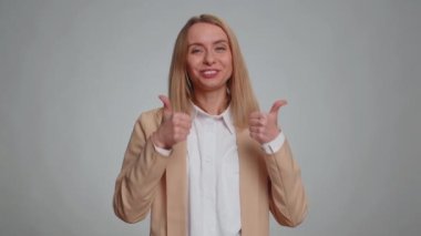 Great job, super. Portrait of young businesswoman showing thumbs up and nodding in approval, clapping hands, successful good work, celebrate win. Female girl in suit. Woman isolated on gray background