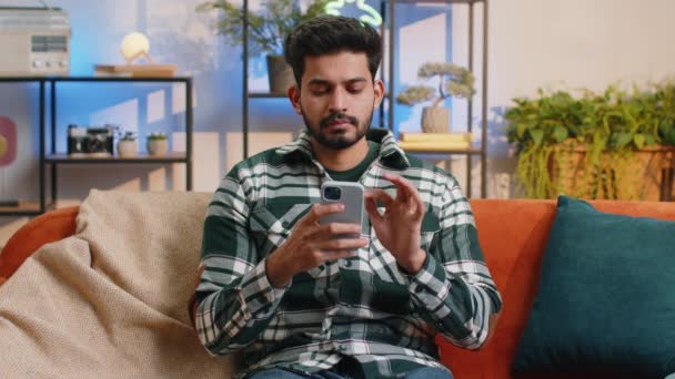 Indian Man Sitting Sofa Uses Mobile Phone Smiles Home Living — Stockvideo