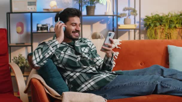 Happy Overjoyed Hindu Indian Man Wireless Headphones Relaxing Sits Couch — Stockvideo