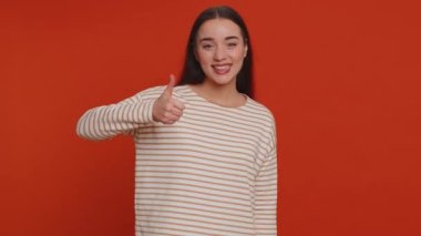Like. Hipster one pretty woman in pullover raises thumbs up agrees with something or gives positive reply recommends advertisement likes good. Young girl isolated alone on red studio background