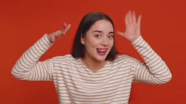 Funny joyful sincere woman 20 years old in pullover making playful silly facial expressions and grimacing, fooling around showing tongue. Young lovely pretty girl isolated alone on red background