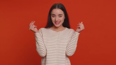Cheerful rich millennial woman showing wasting or throwing money around hand gesture, more tips dreaming about big profit body language. Young millionaire girl isolated on red studio wall background