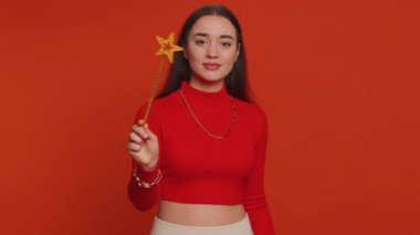Magician witch woman gesturing with magic wand fairy stick, making wish come true, casting magician spell, advertising holidays sale discount. Young pretty girl isolated on red studio background