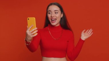 Güzel bir genç kadın etkili blogcu akıllı telefondan selfie çekiyor, internetten video görüşmesi yapıyor, aboneler için yeni sosyal medya vlog hikayeleri kaydediyor. Kırmızı stüdyo arka planında izole edilmiş kız
