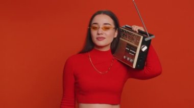 Lovely woman using retro tape record player to listen music, disco dancing of favorite track, having fun, entertaining, fan of vintage technologies. Young adult girl isolated on red wall background