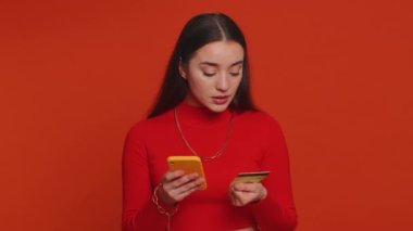 Para transferi, online alışveriş, ödeme yaparken kredi kartı ve akıllı telefon kullanan samimi, güzel bir bayan müşteri. Finans ve internet. Genç kız kırmızı arka planda tek başına.