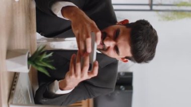 Indian businessman playing on smartphone exciting mobile application celebrate winning racing or shooter game at office desk workplace. Professional freelancer man enjoy good work of new app. Vertical