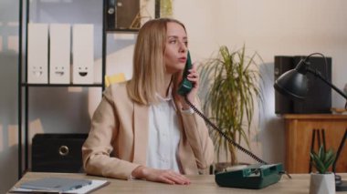 Blonde young businesswoman working, having talk with client on retro old-fashioned wired telephone at home office workplace desk. Saleswoman in formal suit. Remote distant job. Employment occupation