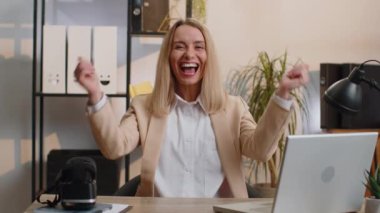 Money cash dollar rain falling on happy young businesswoman celebrating success, winning goal achievement good news lottery jackpot luck at home office workplace desk. Career grow. Girl in formal suit