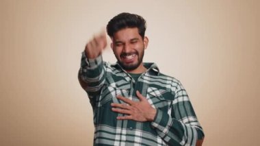 Amused bearded indian man pointing finger to camera, laughing out loud, taunting making fun of ridiculous appearance, funny joke anecdote. Handsome hindu guy isolated alone on beige studio background