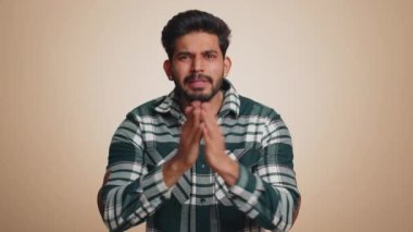 Please, God help, forgive me. Indian man praying, looking upward and making wish, asking with hopeful imploring expression, begging apology. Handsome hindu guy isolated on beige studio background