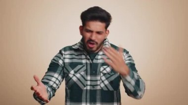 Indian man in shirt screams yell from stress tension problems feels horror hopelessness fear panic surprise shock expresses gestures rage. Handsome hindu guy isolated on beige studio background
