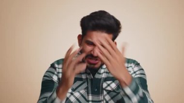 Bearded indian man fingers crossed, feeling hopelessness, loneliness, nervous breakdown, loses becoming surprised by lottery results, bad fortune, loss, unlucky news. Hindu guy on beige background