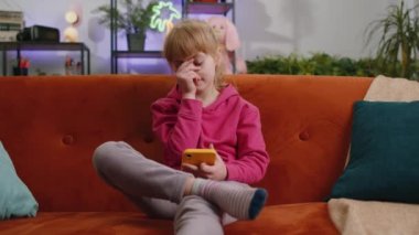 Child kid girl use smartphone, playing game, loses becoming surprised sudden lottery results, bad news, fortune loss, fail education study test. Female teen toddler at home in living room sits on sofa