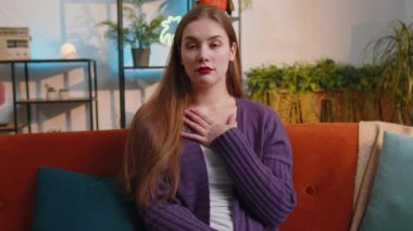 I dont know what to say. Confused pretty woman feeling embarrassed about ambiguous question, having doubts, no idea, being clueless and uncertain at home. Portrait of girl sits on sofa in living room